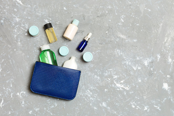 女人化妆包与一套美容产品和身体护理霜在灰色水泥背景与复制空间为您设计图片下载