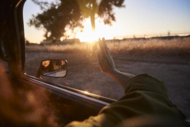 年轻女子在公路上与手臂在日落窗外图片下载