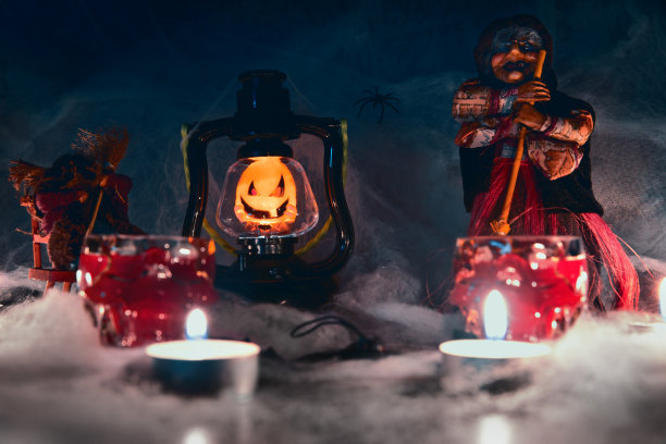 万圣节的背景，壁纸。万圣节南瓜灯——杰克的灯，旁边是女巫的塑像，前景模糊，蜡烛和骷髅形状的眼镜图片下载