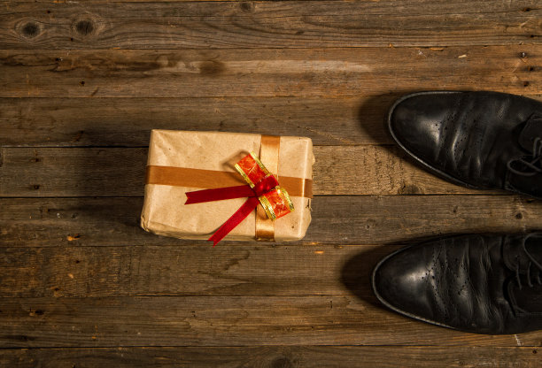概念照片——一个孩子亲手包裹的父亲节礼物放在木地板上粗糙的男鞋旁边图片下载
