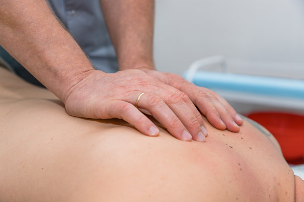 按摩师为男人提供治疗性按摩。男人的双手给耐心的男人做背部按摩。临床接受按摩的男性患者。男人在按摩床上休息图片下载