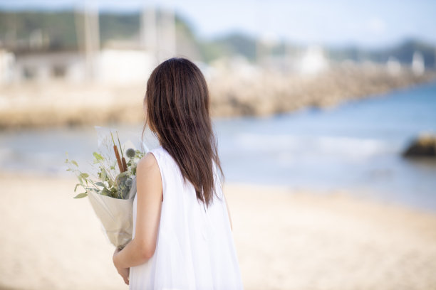 后视图的年轻女子走在海滩上，手持花束图片下载
