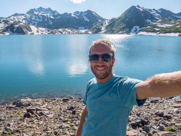 年轻男人在美丽的阿尔卑斯湖边徒步旅行时自拍图片下载