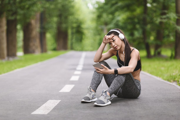 疲惫的亚洲跑步女孩在慢跑后在公园的小路上休息图片下载