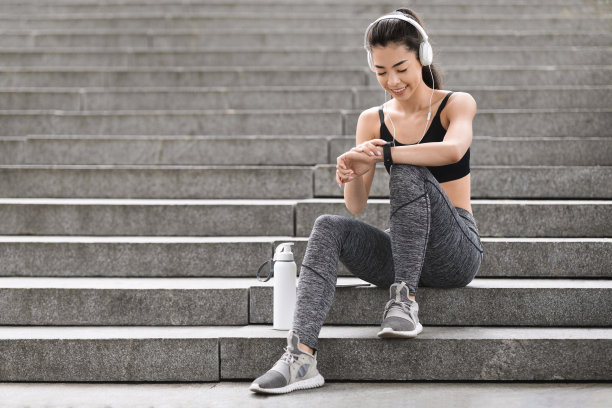 城市体育的概念。微笑的亚洲女孩在户外慢跑前查看智能手表设置图片下载