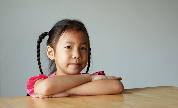 一个亚洲小女孩双臂交叉坐在桌子上图片下载