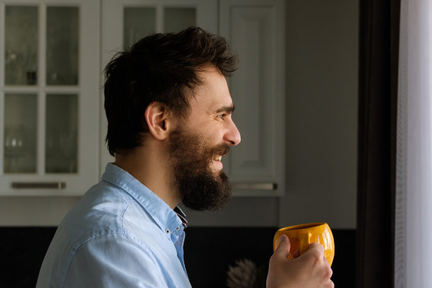 一个留着胡子的男人，手里拿着一个大杯子，在家微笑着图片下载