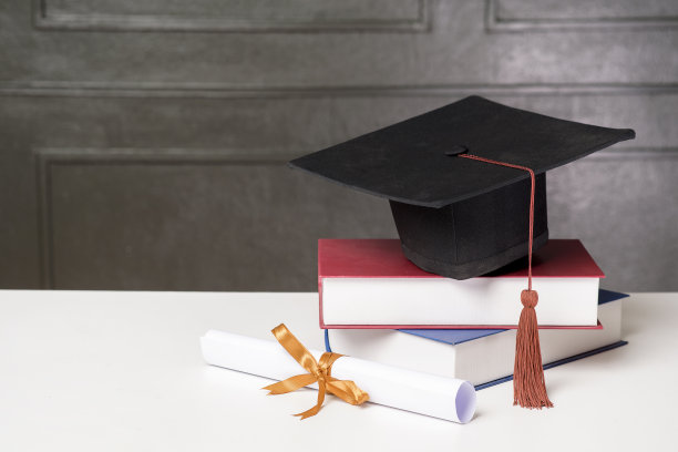 白色课桌上放着毕业帽和书，学历图片下载