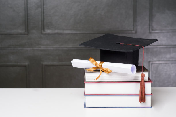 白色课桌上放着毕业帽和书，学历图片下载