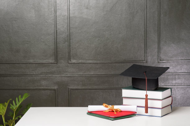 白色课桌上放着毕业帽和书，学历图片下载