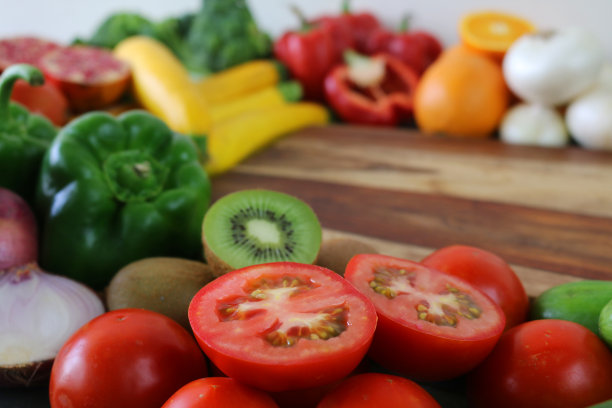 一组完整的和对半的水果和蔬菜放在木砧板上的图片，猕猴桃，青椒，番茄，西葫芦，红洋葱，橙子，石榴和红辣椒，重点放在前景图片下载