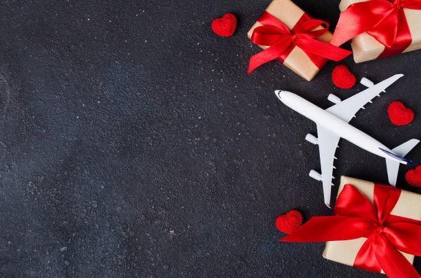假日旅行计划。旅行的概念。飞机模型，礼品盒和红色的心在黑暗的背景。图片下载