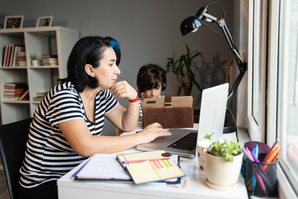 亚洲母亲在家用笔记本电脑工作，儿子在用数码平板电脑图片下载