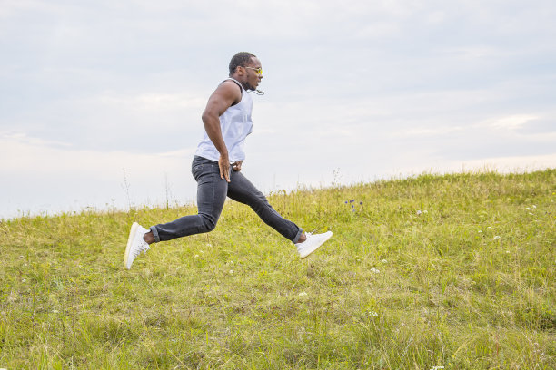 一个年轻强壮的男人在绿色的草地上运动。那家伙又跑又跳。图片下载