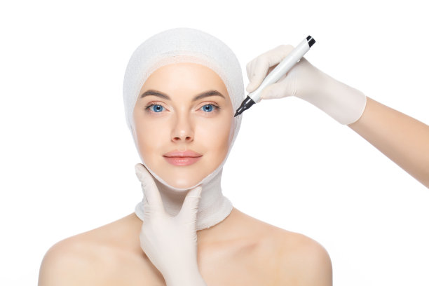 年轻美丽的女性与头部包裹，准备整形手术的医生使用皮肤标记，孤立在白色背景。美实践概念图片下载