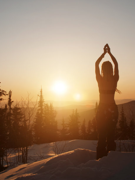 女子站在雪地上，在冬季日出，做早晨冥想的莲花姿势图片下载