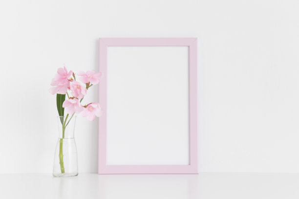 粉红色框架模型与粉红色夹竹桃在玻璃花瓶在白色的桌子上。肖像取向。图片下载