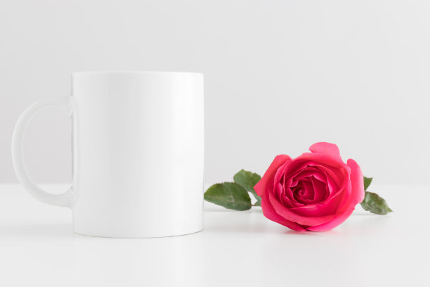 白色桌子上放一朵粉红玫瑰的马克杯模型。图片下载