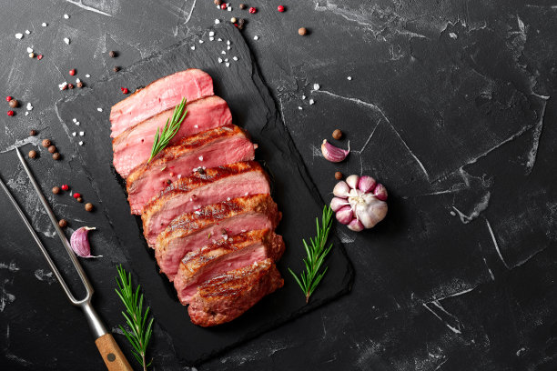 半熟的肋眼牛排，配上香料和香草，以黑石为背景。俯视图，平放，复制空间。图片下载