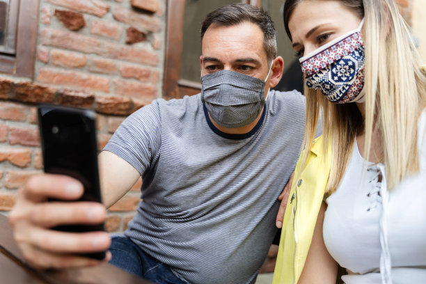 情侣戴着防护口罩在餐厅户外自拍——两名朋友一男一女坐在社交网络上拍手机照片——新常态新冠肺炎概念图片下载