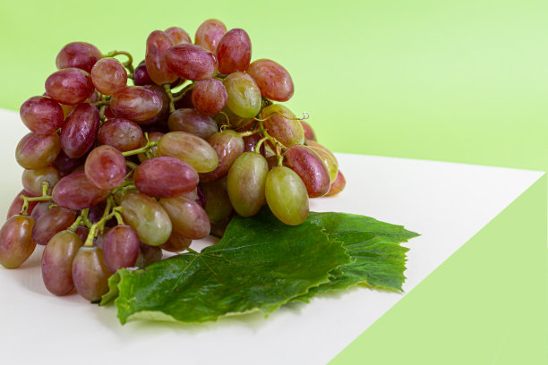 大而淡的葡萄酒葡萄。它被一层白色的酵母覆盖。杯子里盛的是淡葡萄酒。水滴在浆果上。在一个多色的背景上。图片下载