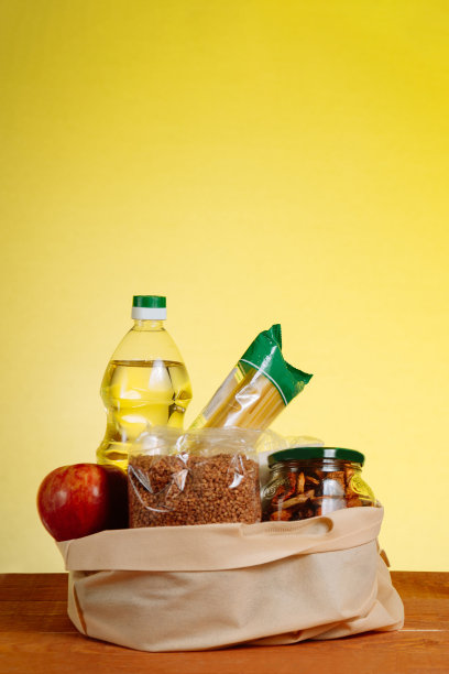 木桌上，黄色背景上，纸袋装着不同的食物。超市购物的概念图片下载