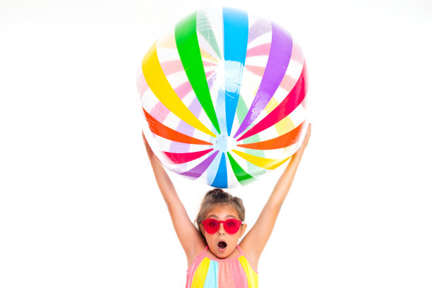 惊讶的女孩戴着太阳镜拿着一个充气彩色条纹球在自己的白色背景图片下载