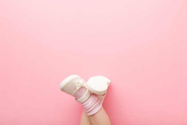 交叉的婴儿腿在白色的鞋子在浅粉色的地板背景。柔和的颜色。特写镜头。文本的空位置。自顶向下的观点。图片下载