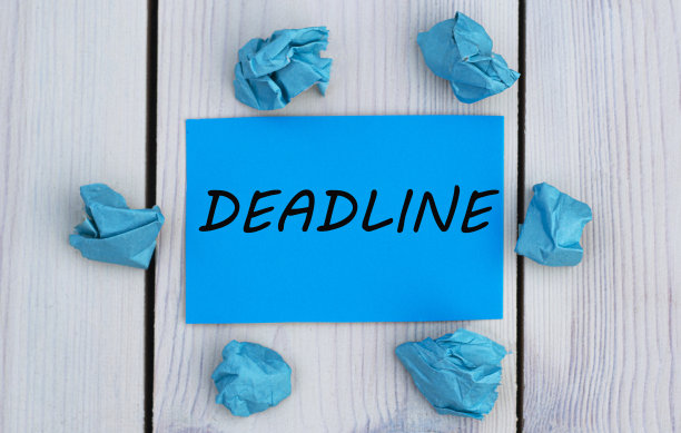 最后期限-字在蓝色纸上，在灯光背景和皱巴巴的纸图片下载