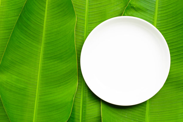 空白的白色陶瓷板上芭蕉叶背景。图片下载