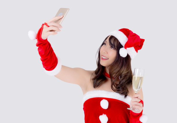 美丽的肖像年轻的亚洲女人在圣诞老人拿着香槟的杯子和自拍在派对上庆祝在白色的背景，圣诞节和新年的概念。图片下载