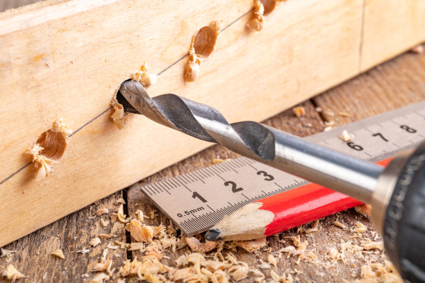 用金属钻在一块木头上钻洞。测量孔间距离的金属尺。光背景。图片下载