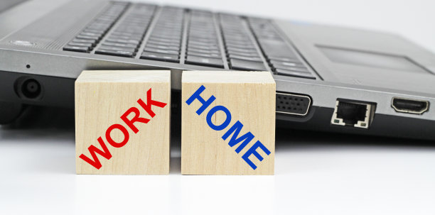 在笔记本电脑的背景上刻有home和work with copyspace的两个木制立方体:在家工作和在家工作的概念。图片下载