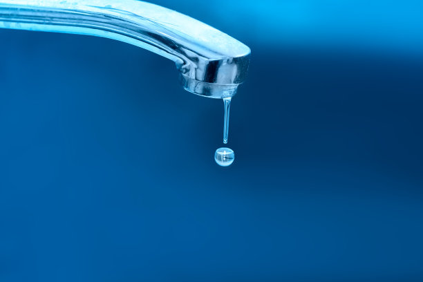 水滴从蓝色背景上的铬水龙头流出。节约用水的理念。图片下载
