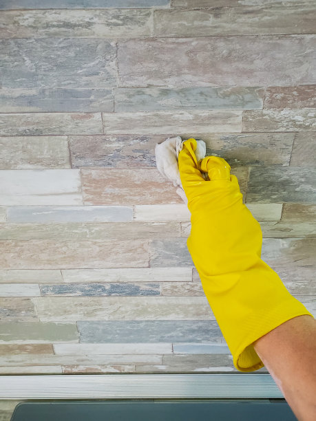 手拿一只黄色橡胶手套，拿着一块抹布，在厨房里清洗墙壁图片下载