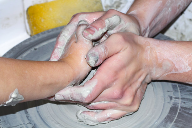 教陶艺，一个师傅的手和一个孩子在陶艺轮上。图片下载