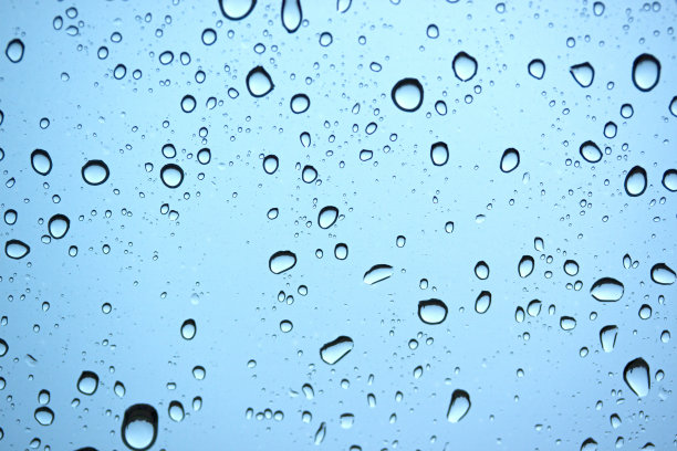 在雨季，蓝色背景上的自然雨水滴在汽车玻璃上。图片下载