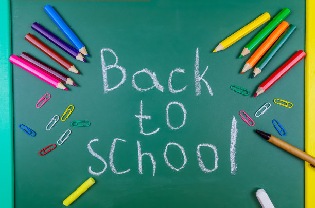 在黑板上，它是用粉笔写回学校，旁边的回形针，粉笔，钢笔，铅笔，俯视图。美丽，明亮，有趣的学校背景。图片下载