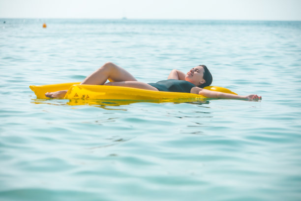 美丽性感的女人躺在黄色充气床垫在海水图片下载