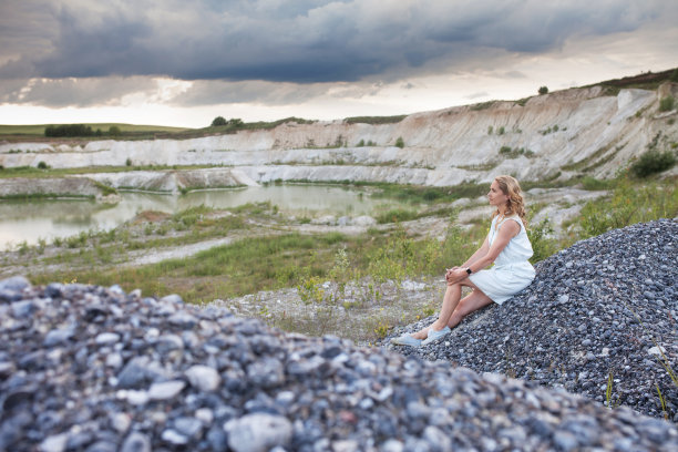 年轻女子坐在石山上，背对着沙丘。美丽的自然景观图片下载