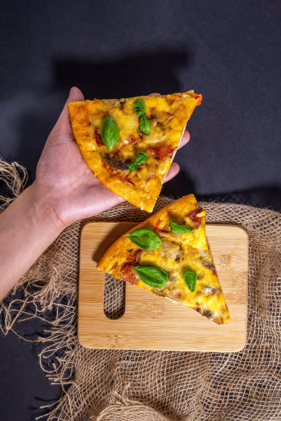 罗勒叶在黑色背景，俯视图。垂直的照片。有火腿、肉、奶酪、西红柿和蘑菇的披萨。两部分。图片下载