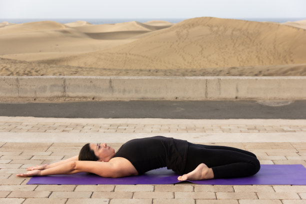 灵活的女人在supta virasana紫色垫子上与Maspalomas沙丘的背景图片下载