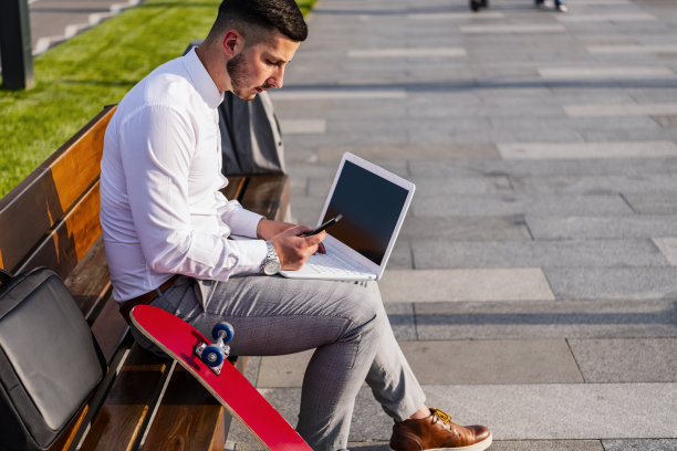 商人坐在滑板旁边的长椅上。图片下载
