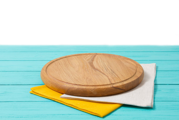 在白色的背景上，蓝色的木桌上放置着圆形的木头披萨切菜板和桌布。俯视图和复制空间，空和模板模型与食物的地方。图片下载