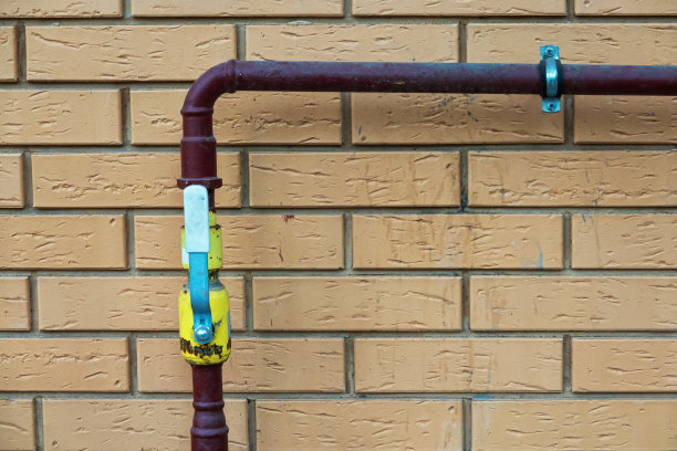 红色的管子连接在砖墙上，有一个直角的转弯。黄色的水龙头开着。背景。纹理。图片下载