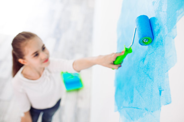 在公寓里修理。快乐的小女孩用蓝色的油漆涂墙，图片下载