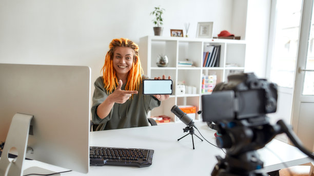 在这里。白天，梳着雷鬼辫的女性科技博主看着摄像头，在录制视频博客或视频博客的同时展示黑屏智能手机图片下载