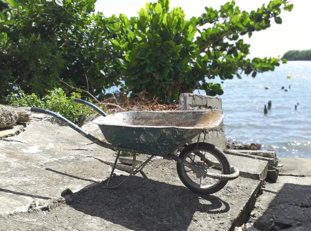 海边建筑物外生锈的、旧的、空的独轮手推车的侧视图。自然环境中的建筑和园艺工具。图片下载