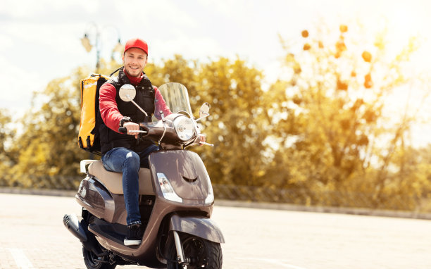 外面骑着摩托车背着黄色背包送食物的快递员图片下载