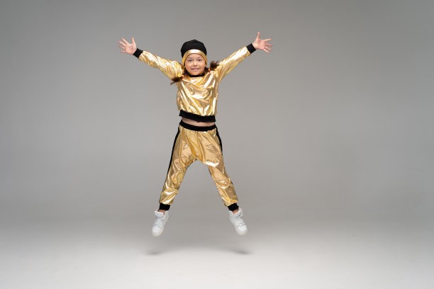 快乐的小女孩在金色套装跳舞孤立在白色的背景。图片下载